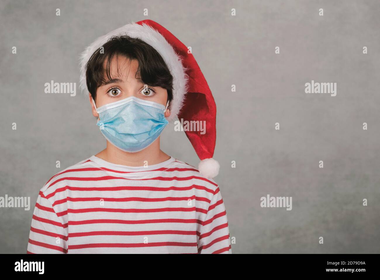 Frohe Weihnachten, Nahaufnahme des Kindes mit medizinischer Maske trägt Weihnachtsmann hut auf grauem Hintergrund Stockfoto