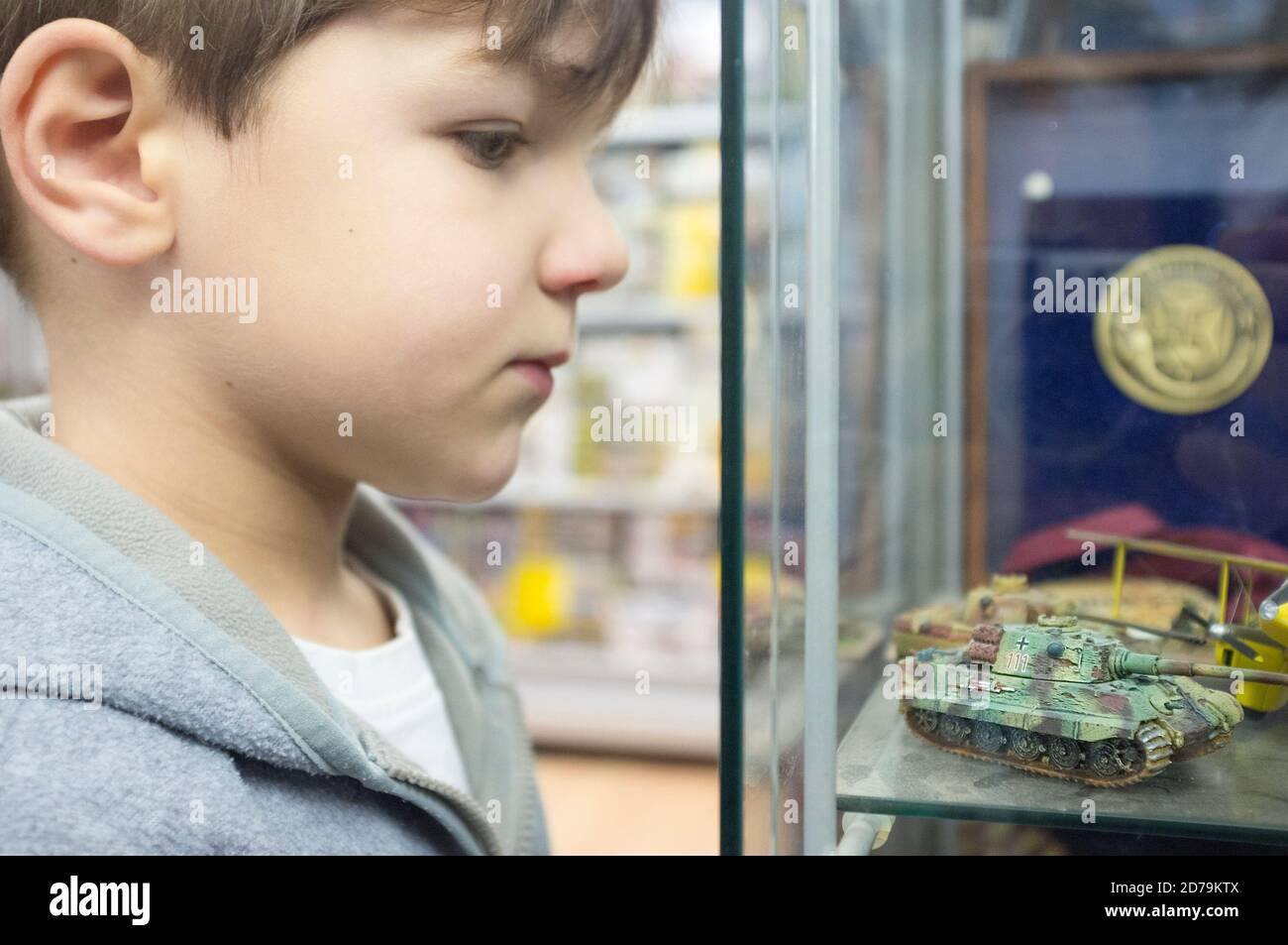 5 Jahre kleiner Junge, der Modellbau des Panzers beobachtet, der am Glasschrank angezeigt wird. Selektiver Fokus Stockfoto