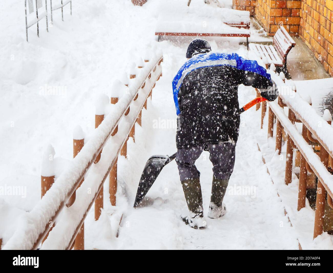 Ein Arbeiter räumt Schnee von der Veranda eines Hauses Bei starkem Schneefall Stockfoto