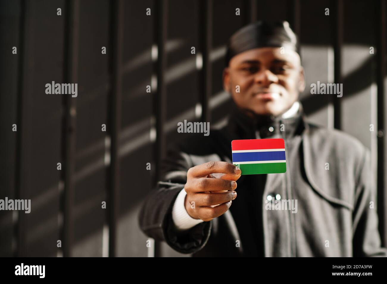 Afrikanischer Mann tragen schwarz durag halten Gambia Flagge bei der Hand isoliert dunklen Hintergrund. Stockfoto