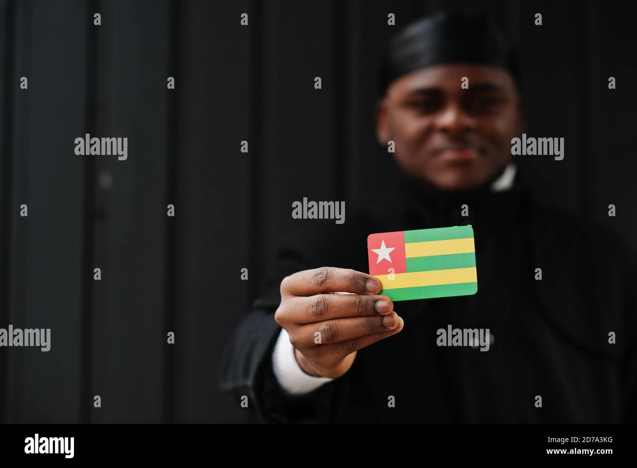 Afrikanischer Mann tragen schwarze durag halten Togo Flagge bei der Hand isoliert dunklen Hintergrund. Stockfoto