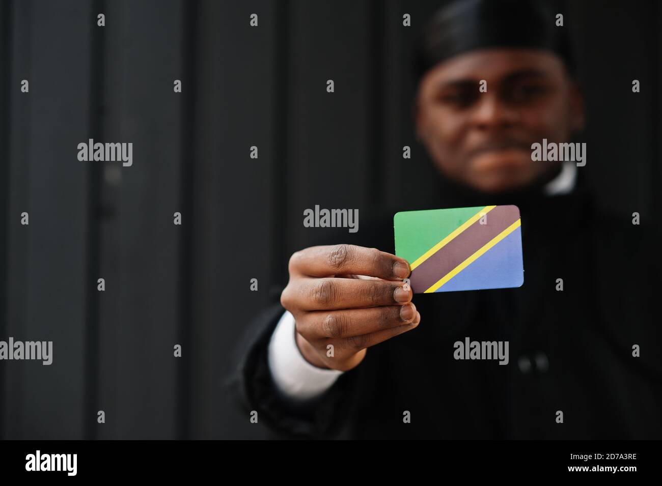 Afrikanischer Mann tragen schwarz durag halten Tansania Flagge bei der Hand isoliert dunklen Hintergrund. Stockfoto