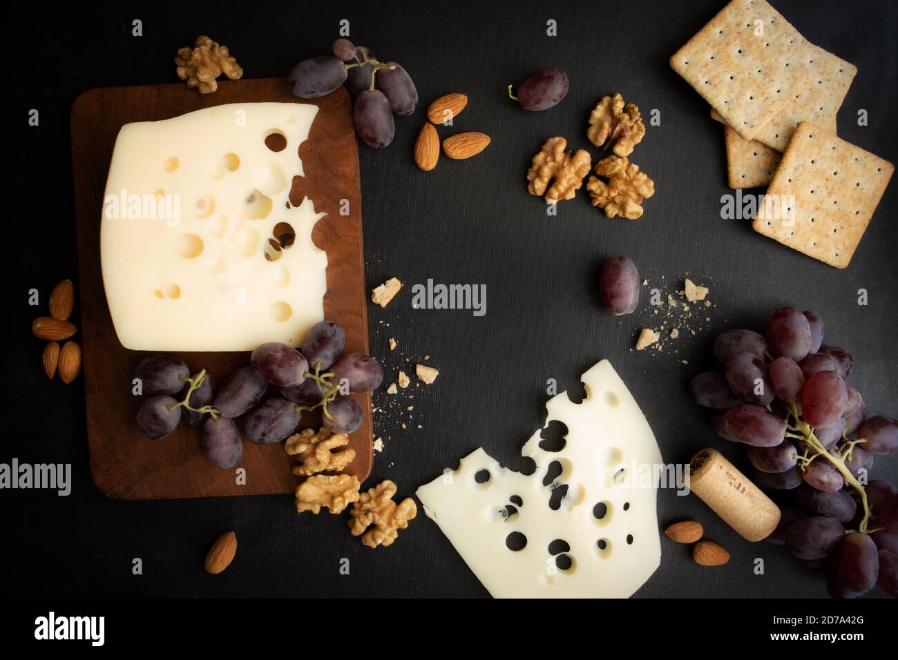 Maasdam Käse, Walnuss, Kekse und Beeren von lila Trauben auf einem dunklen Hintergrund mit Platz für Text. Poster. Stockfoto