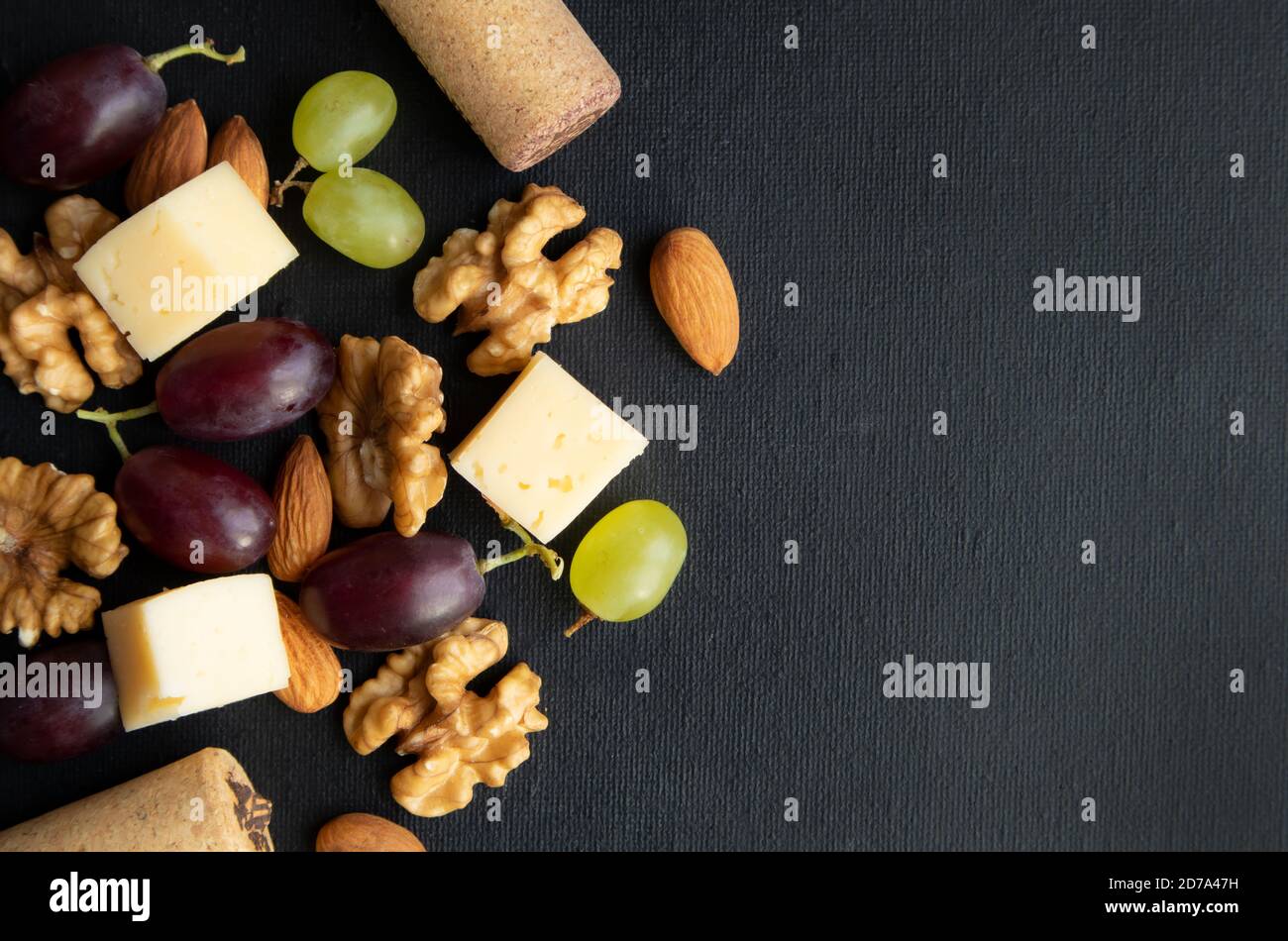 Maasdam Käse. Walnuss und Beeren von lila und grünen Trauben auf einem dunklen Hintergrund mit Platz für Text. Poster. Stockfoto
