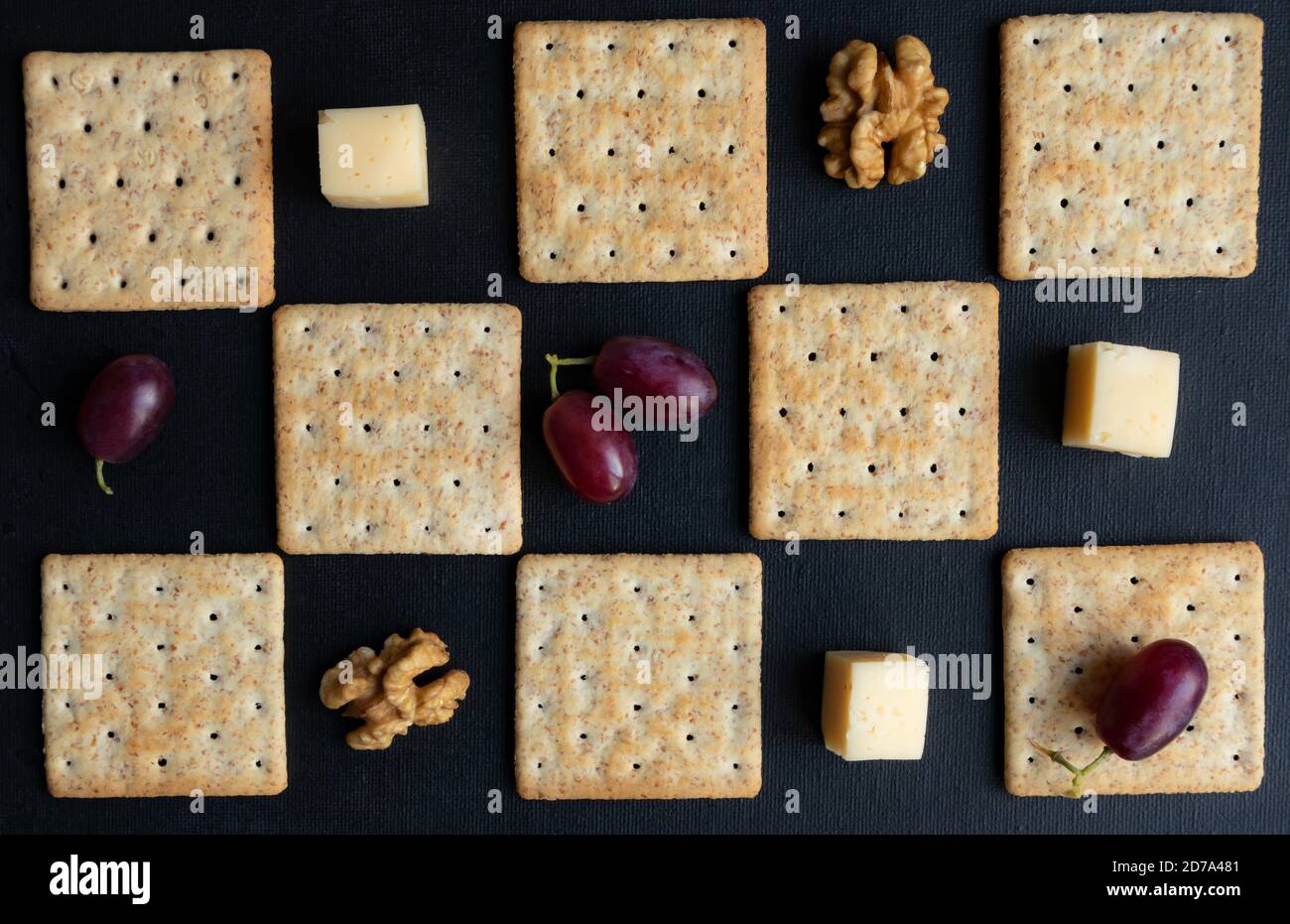 Maasdam Käse, Walnüsse, Kekse und lila Trauben vor einem dunklen Hintergrund gestaffelt. Poster. Stockfoto