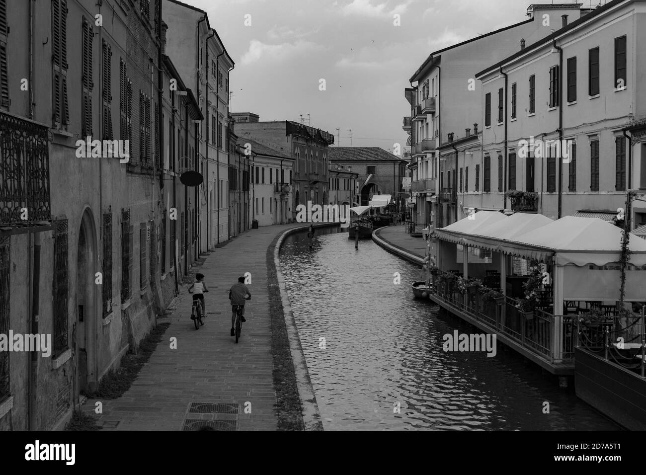Blick auf den Kanal von Comacchio, Häuser mit Kindern, die Fahrräder fahren Stockfoto
