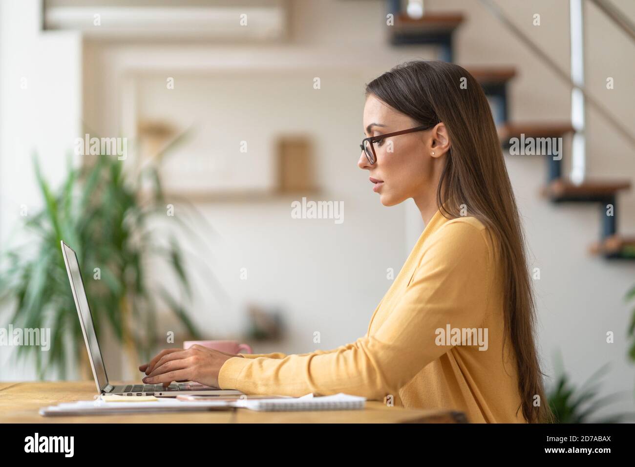 Fokussierte Millennial Frau in Brille sitzt auf dem Tisch, Remote-Arbeit auf Laptop, Analyse von Projekt-Statistiken Informationen, Antworten auf Kunden-E-Mails aus Stockfoto