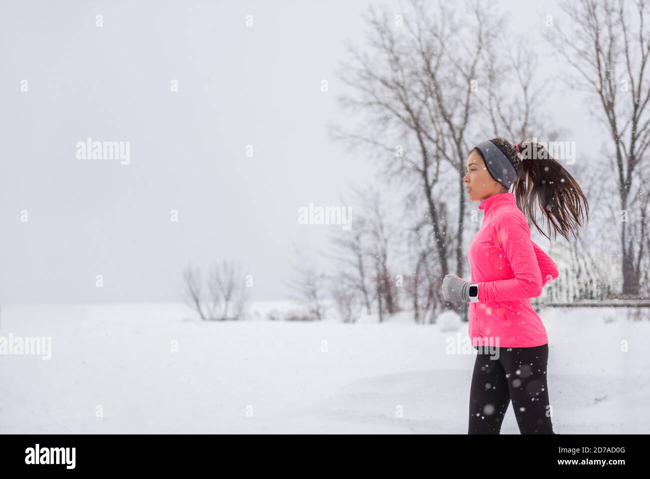 Winter Running Frau bei kaltem Schnee joggen draußen in winddichter Kleidung mit Handschuhen, Stirnband, Winterstrumpfhose und Windjacke in weiß Stockfoto