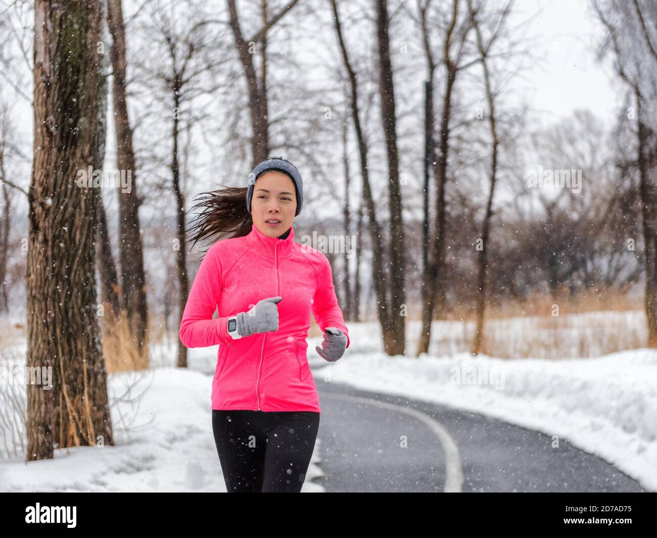 Winter Laufsport Frau in Jacke und Smartwatch. Fit asiatischen Läufer Joggen im Winterwald tun Outdoor-Lauf-Übung. Aktiver Lebensstil. Stockfoto