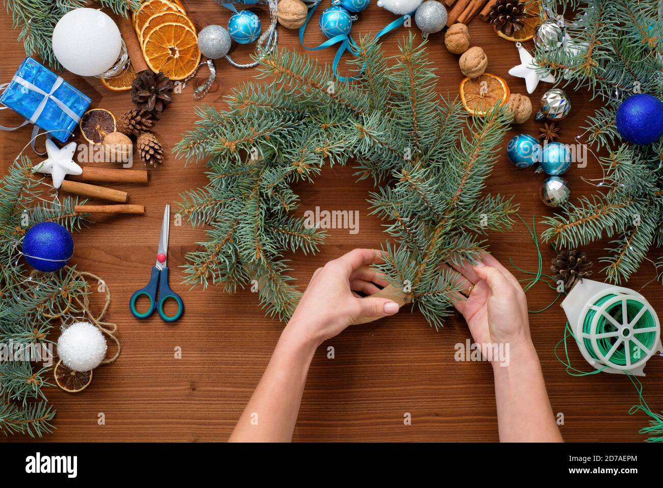 Schritt-für-Schritt-Prozess der Herstellung eines Weihnachtsbaumkranz zu Hause aus Fichtenzweigen, Orangen und Weihnachtskugeln in den silbernen und blauen Farben der Stockfoto