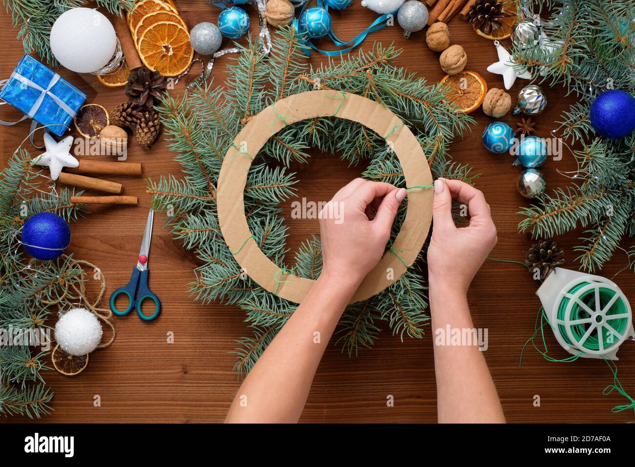 Schritt-für-Schritt-Prozess der Herstellung eines Weihnachtsbaumkranz zu Hause aus Fichtenzweigen, Orangen und Weihnachtskugeln in den silbernen und blauen Farben der Stockfoto