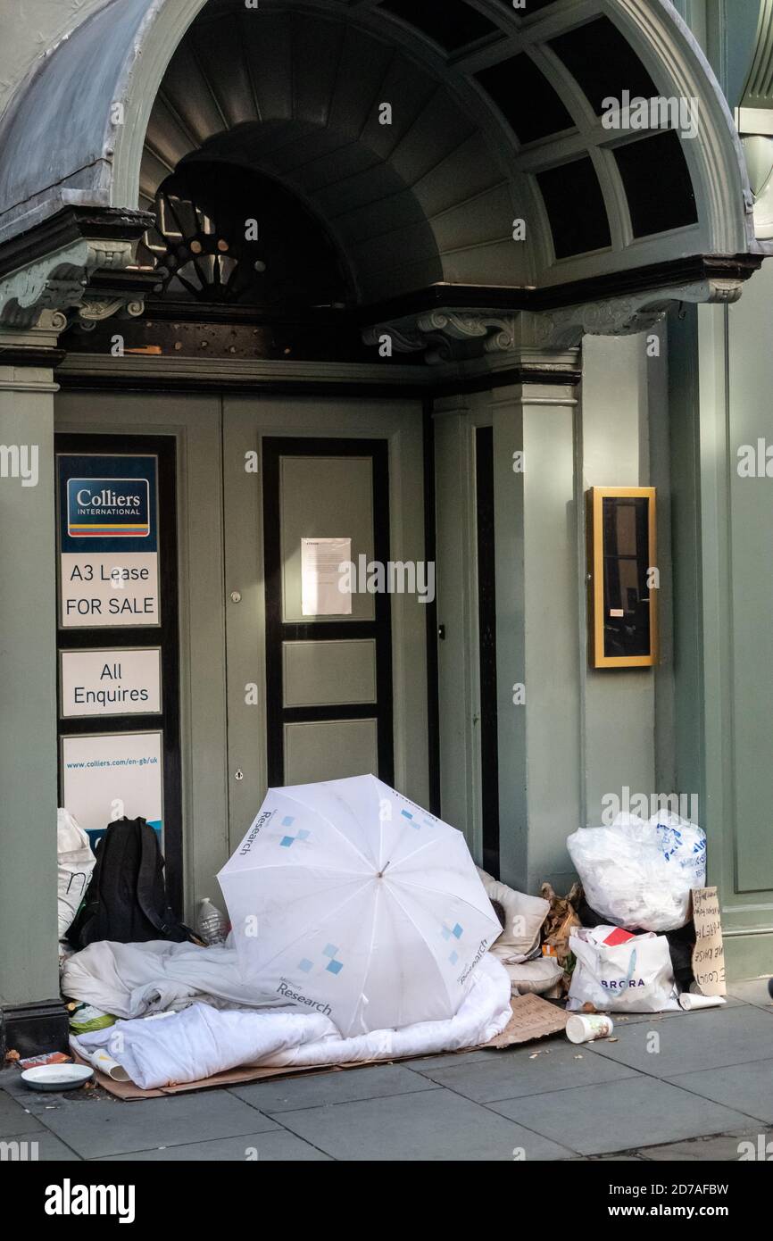 Mann, der in der Tür eines leeren Geschäftsgebäudes schlecht schläft Ein Microsoft Regenschirm leeren MacDonald Container und verschiedene Plastiktüten Stockfoto