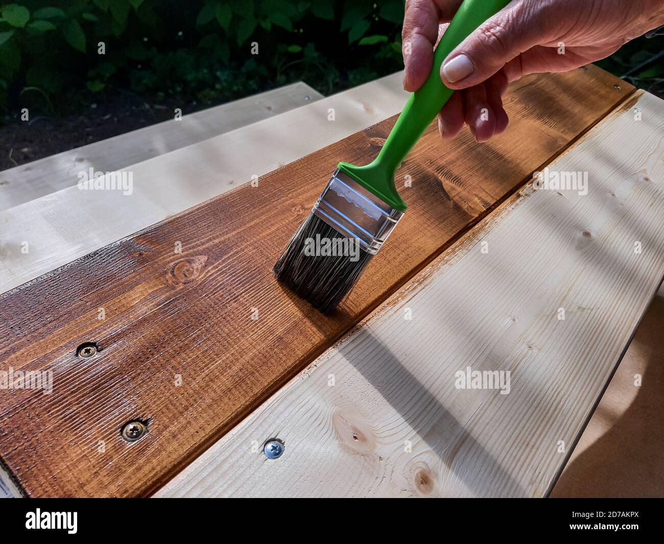 Schutzlack auf einen Holzboden der Terrasse auftragen.Holzarbeiten außen  malen.Hand Verwenden Sie Pinsel Lack klar auf Holzoberfläche  Stockfotografie - Alamy