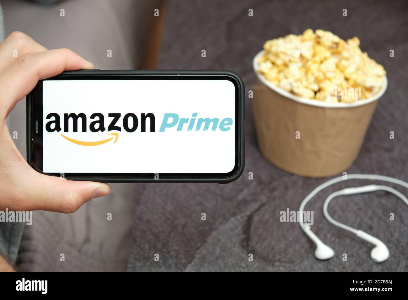 Nahaufnahme mans Hand hält ein Handy mit Amazon Prime Logo mit Apple Kopfhörer und Popcorn-Box neben ihm, August 2020, San Francisco, USA Stockfoto