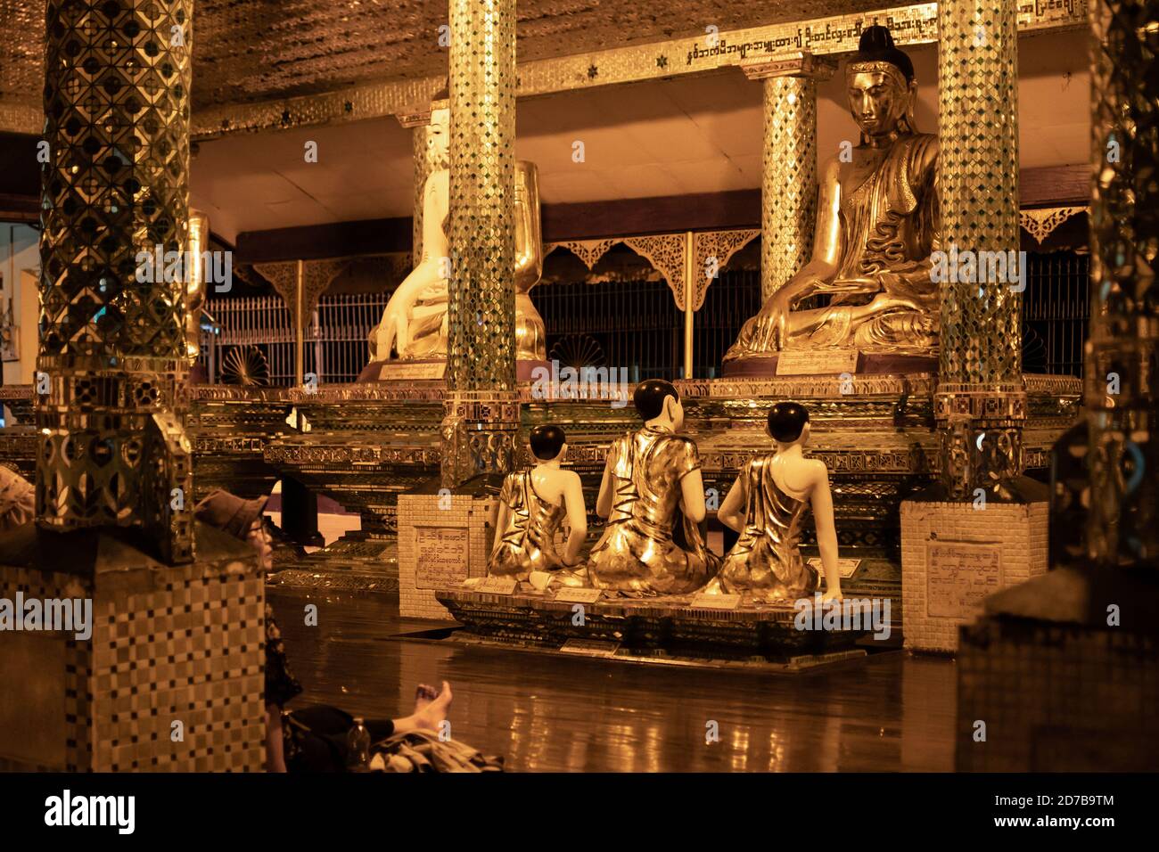 Yangon, Myanmar - 30. Dezember 2019: Sitzen goldene buddha-Statuen in einem gelb reflektierenden Raum mit dekorativen Säulen an der Shwedagon Pagode Stockfoto
