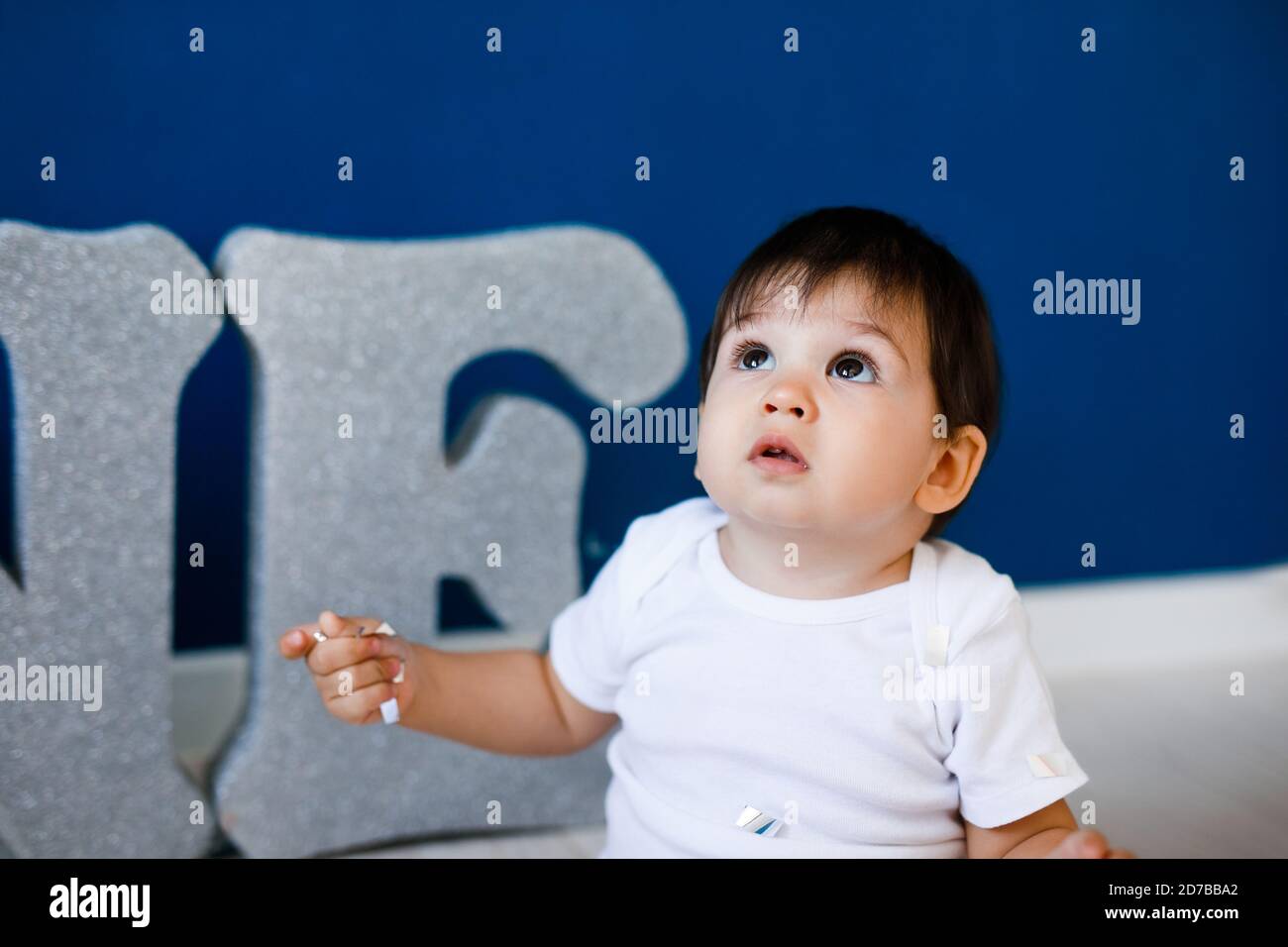 Ein Jahr alter Junge feiert Geburtstag in der Nähe von silbernen Buchstaben EINE auf blauem Hintergrund mit Sternen. Stockfoto
