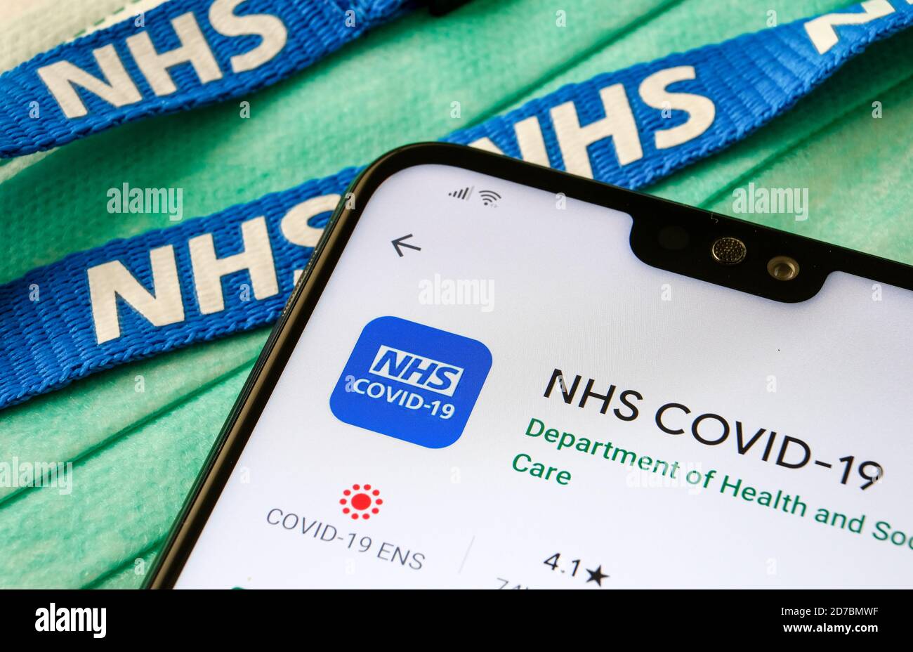 NHS COVID-19 App im Play Store auf dem Bildschirm des Smartphones neben viralen Masken und NHS Lanyard gesehen. Stockfoto