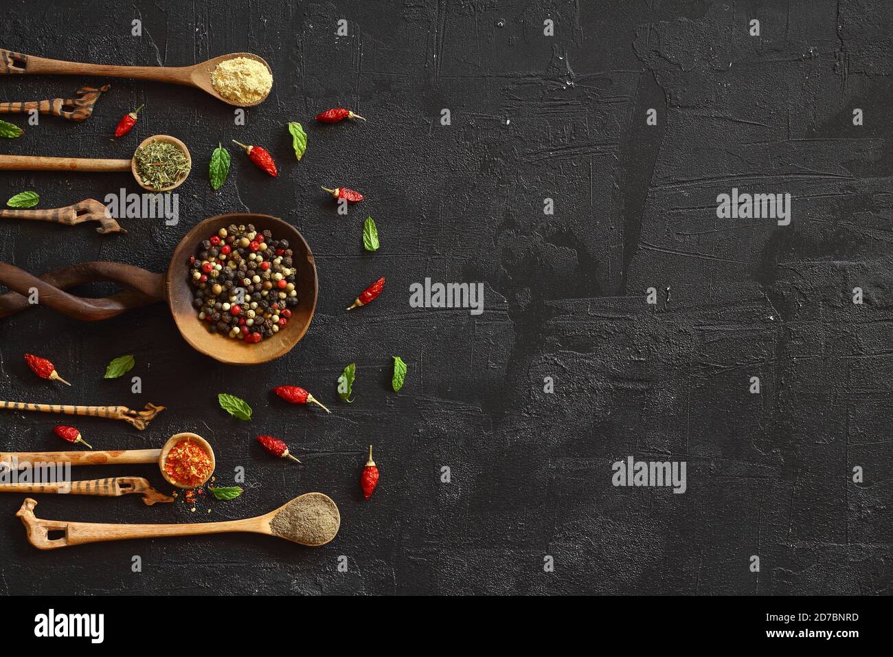 Verschiedene Arten von Gewürzen auf einem schwarzen Stein. Orientalische Gewürze in Löffeln, Paprika, Currypulver, Kräuter auf schwarzem Metallblech im asiatischen Stil. Flache Lay, Stockfoto