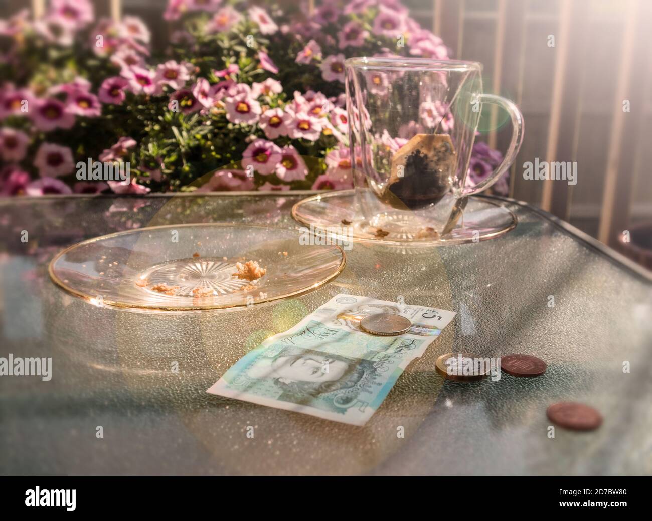 Britische Währung auf dem Tisch, Trinkgeld, Untertasse aus Glas und Tasse Tee, Nachmittagsambiente. Stockfoto