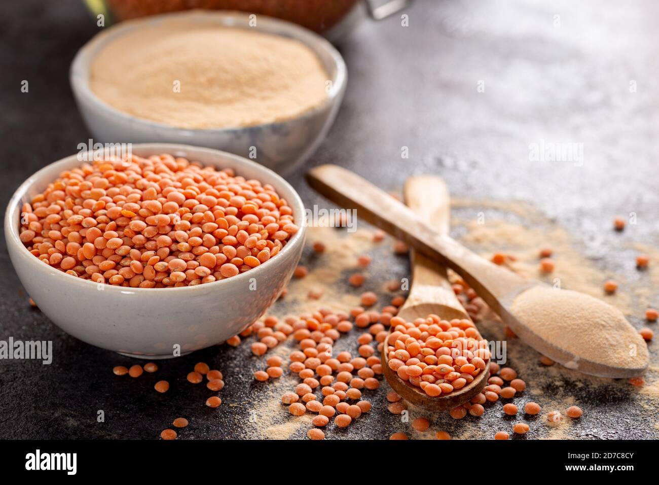 Rote Linsen und Linsenmehl in Schüssel auf dunklem Grund. Stockfoto