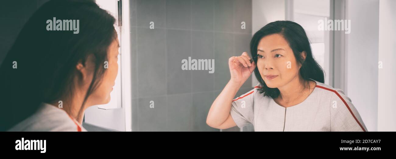 Make-up-Spiegel asiatische Frau mittleren Alters Anwendung Mascara Make-up in Badezimmer Panorama Banner Home Lifestyle Hintergrund Stockfoto