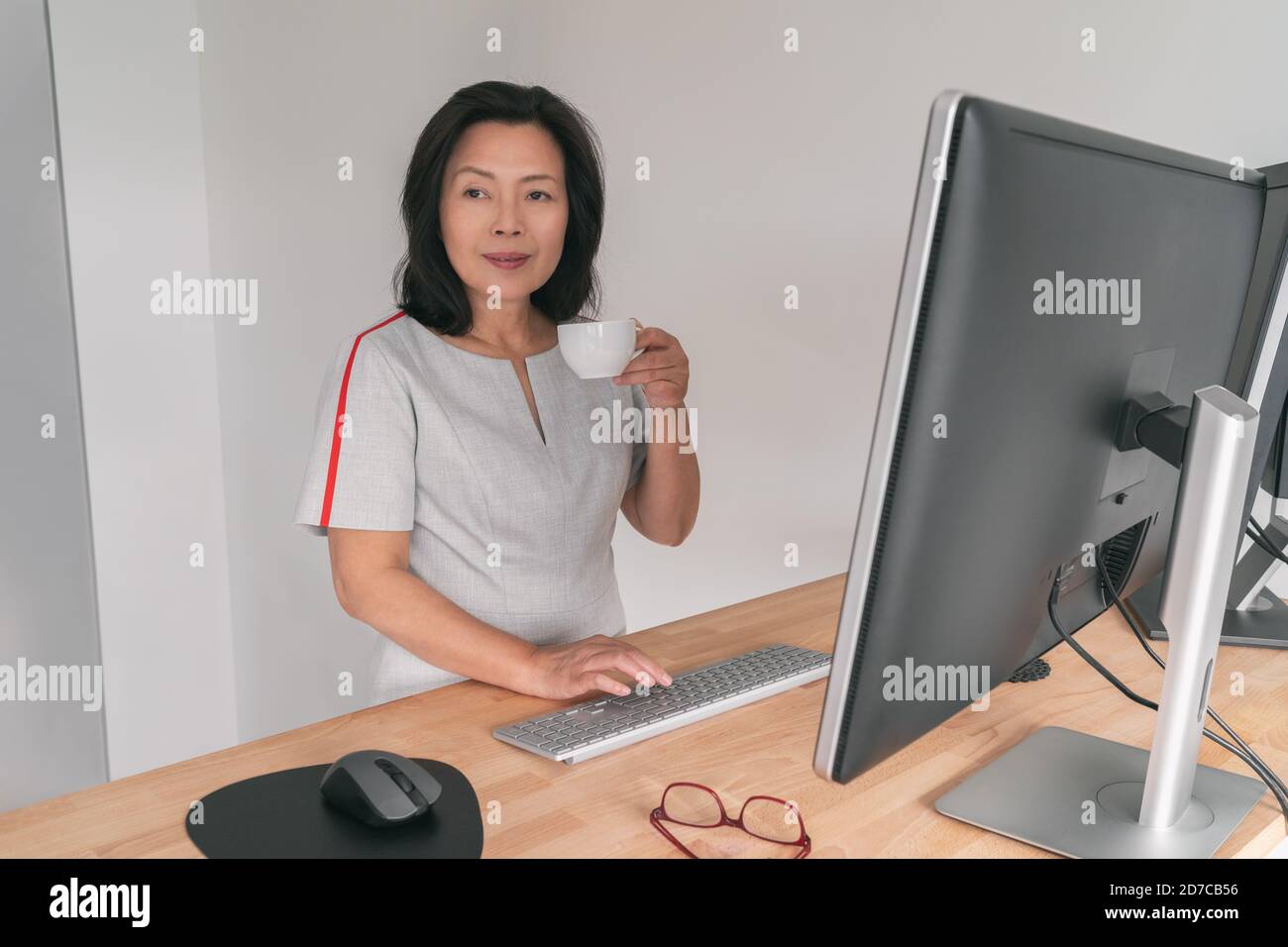 Reife asiatische Geschäftsfrau arbeiten auf Stehtisch zu Hause Büro trinken Kaffeetasse eine Pause businesswoman professionelle Dame Bei der Arbeit tippen Stockfoto