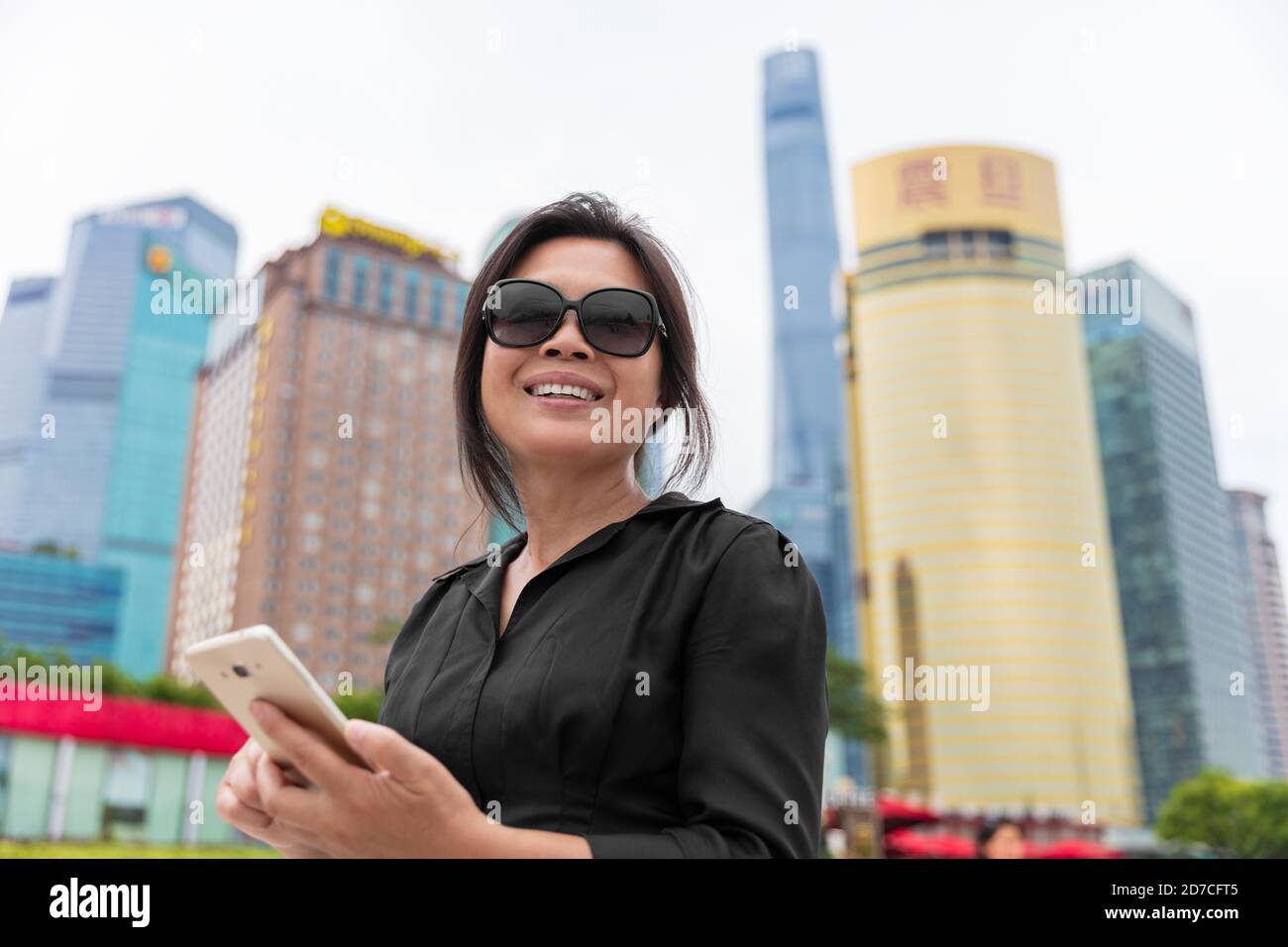 Asiatische Geschäftsfrau Immobilienmakler mit Handy-SMS in Shanghai Stadt, China. Glücklich lächelnd reife Dame arbeiten auf Smartphone im Freien Stockfoto