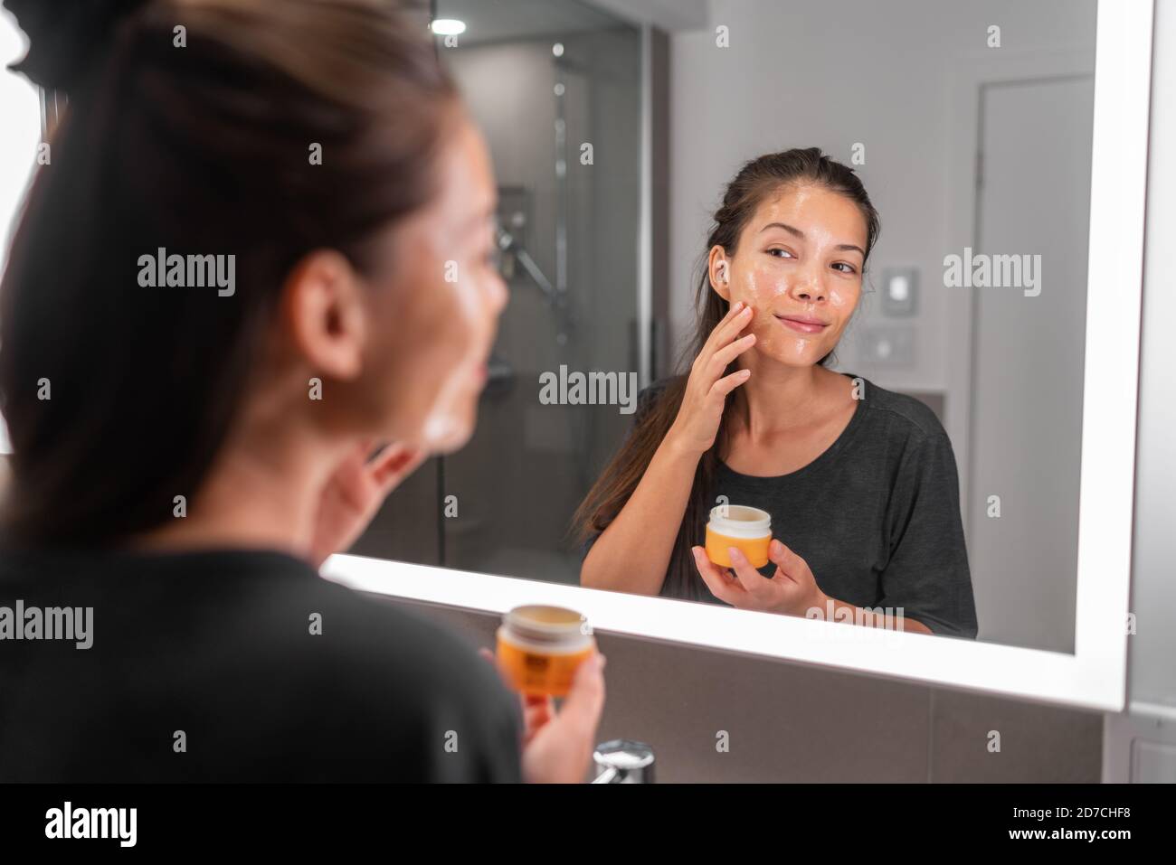 Hautpflege Frau Putting Gesichtsmaske Produkt Reinigung Hautpflege Schönheit Lifestyle - asiatische Frau suchen in LED-Spiegel im Badezimmer Anwendung Gesichtsreiniger Stockfoto