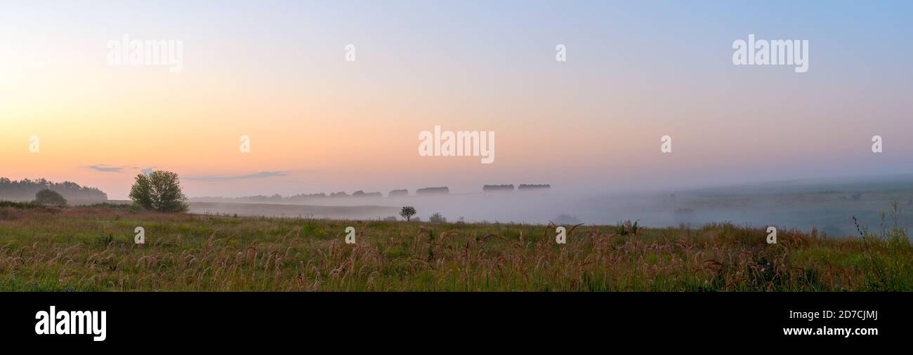 Panoramablick auf Felder und grüne Hügel bei Nebel sonnenaufgang Stockfoto