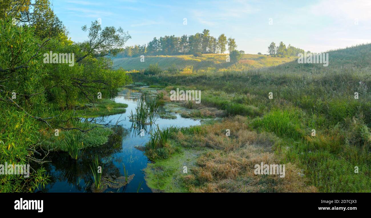 Ruhige, neblige Landschaft mit kleinem Fluss bei Sonnenaufgang Stockfoto