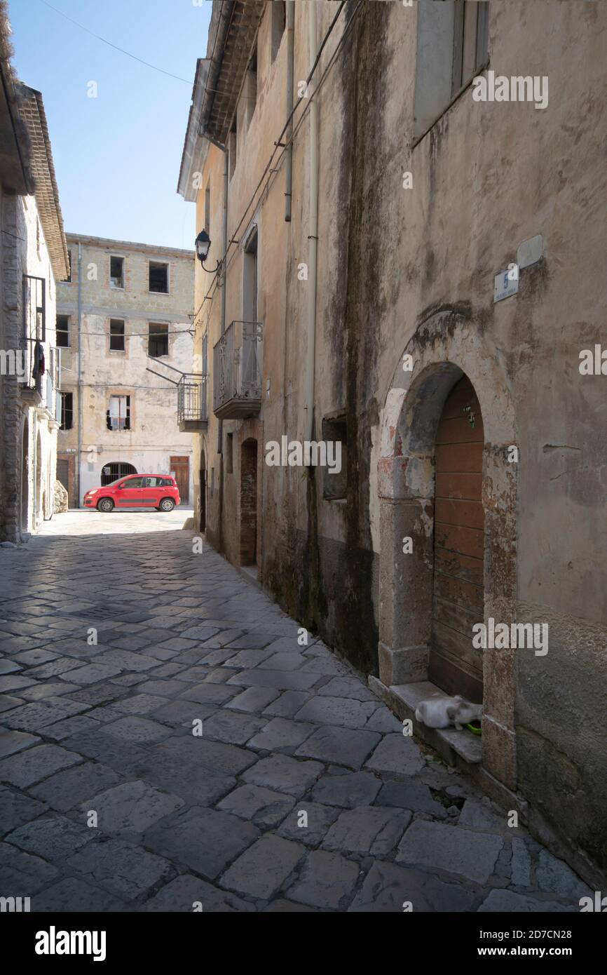 Schmale Straße in alten Turm von Fondi mit einem roten Geparktes Auto auf dem Hintergrund und eine Katze essen in Der Vordergrund Stockfoto