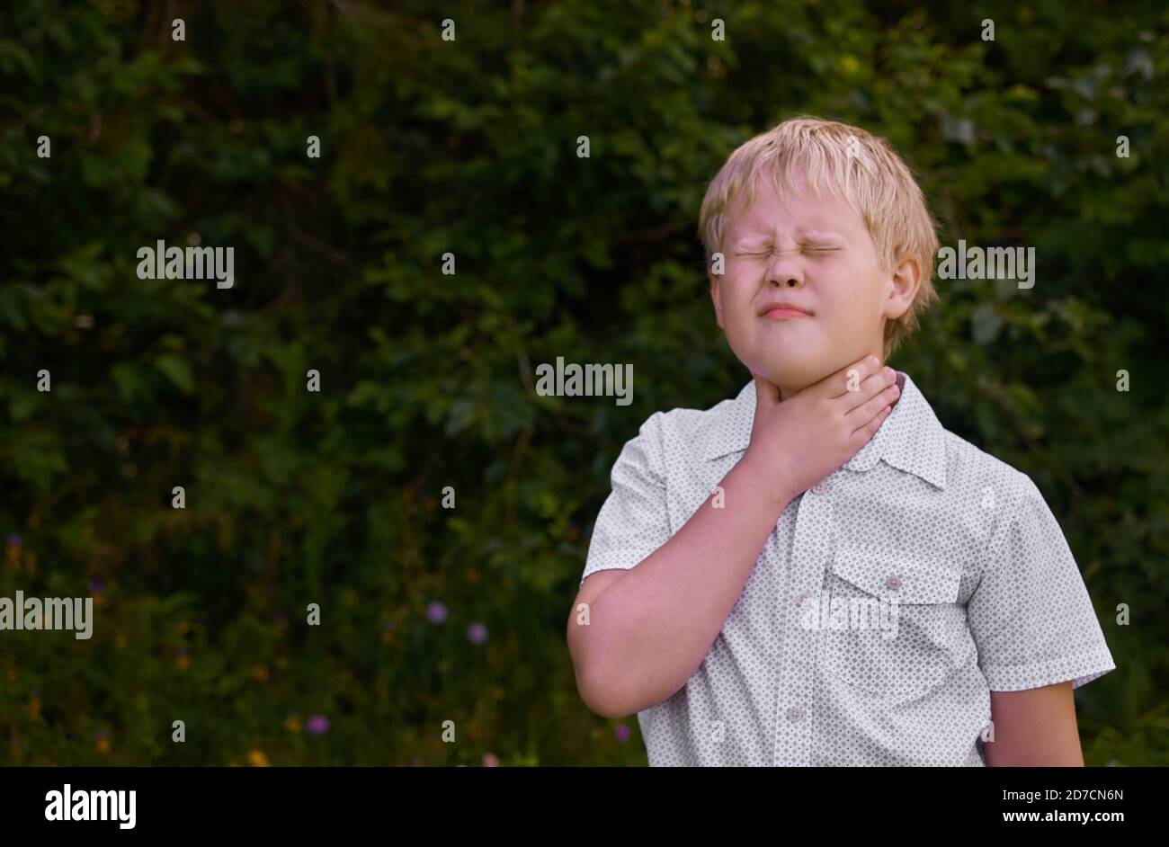 Der Junge hält seine Hand an seine Kehle und zuckt Am Schmerz im Park Stockfoto