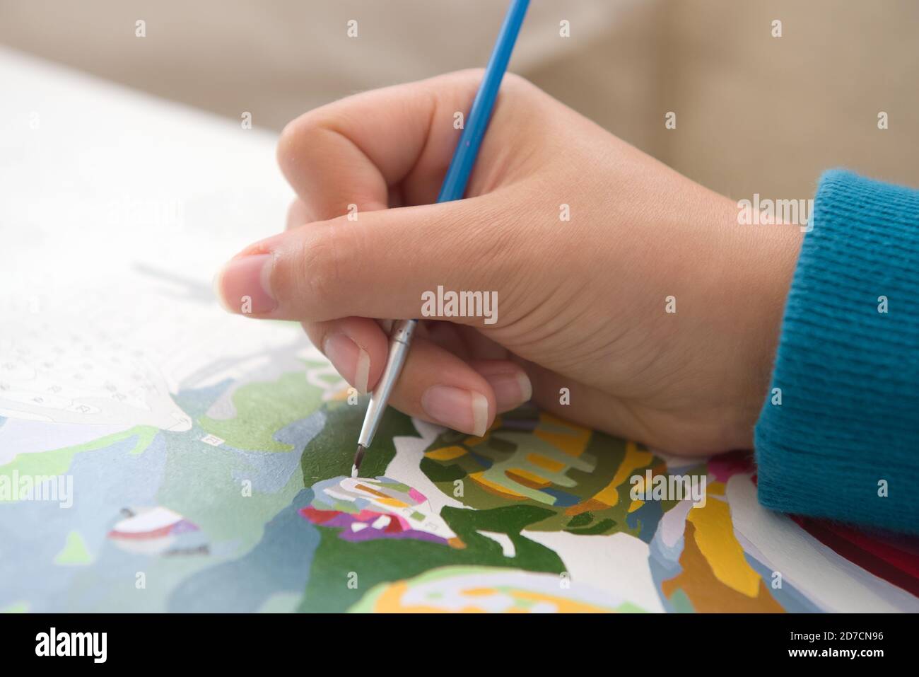 4 - Junge und Jugendliche weibliche Hand mit natürlichen Nägeln ist in großem Detail mit einem blauen Pinsel und Malerei durch Zahlen gezeigt. Ein beliebtes Hobby. Stockfoto