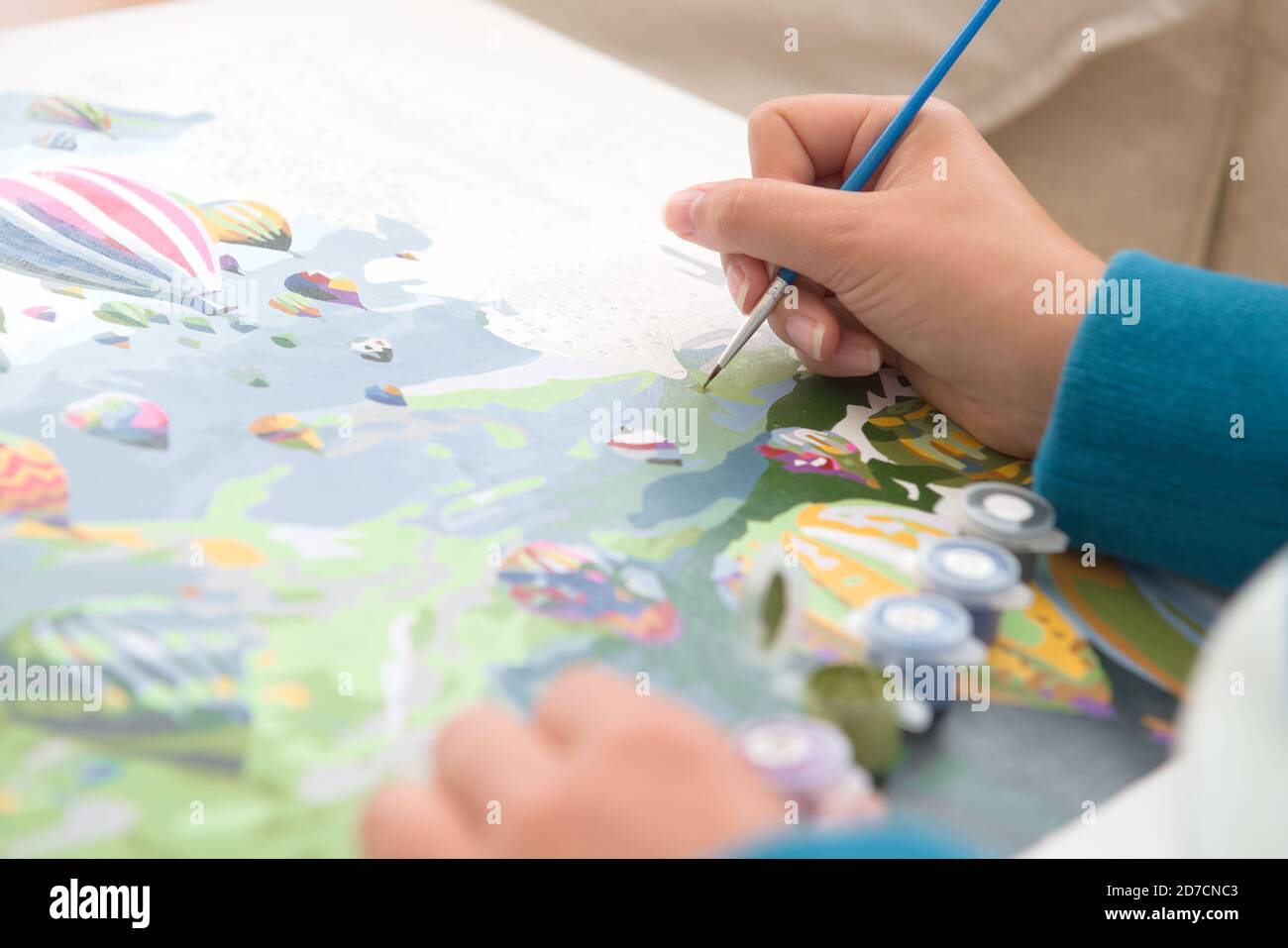 11 - Heißluftballon Malerei durch Zahlen Kunstwerk. Gemalt von jungen Menschen mit gebräunter Haut. Blaue Pullover- und Pinselfarben knallen auf die Haut Stockfoto