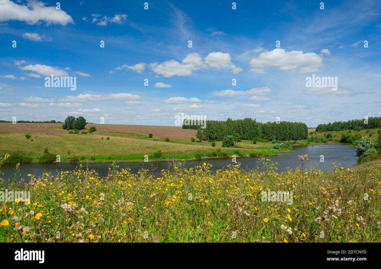 Sonnige Sommerlandschaft mit Fluss, grünen Hügeln und schönen Wolken in blauem Himmel. Stockfoto