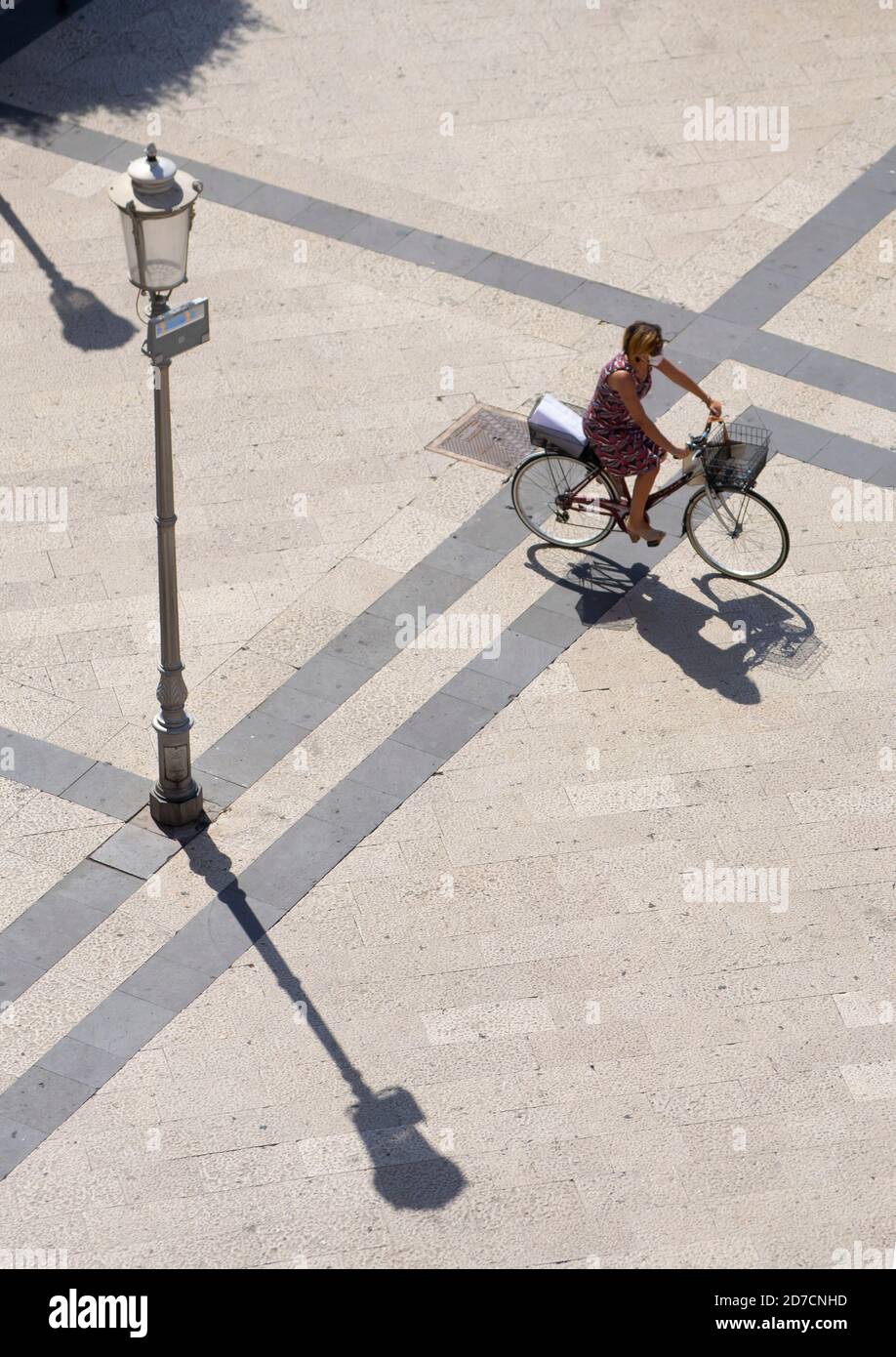 Eine Dame fährt mit dem Fahrrad unter der Sommersonne hinein Ein Platz in der Stadt Fondi Stockfoto
