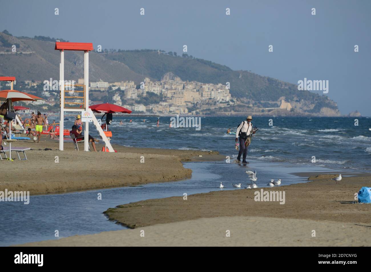 Ein freier Strand in der Nähe von Sperlonga im Sommer 2020. Ein nicht-EU-Bürger spaziert beladen mit Gegenständen, die er Badegäste zum Verkauf anbietet Stockfoto