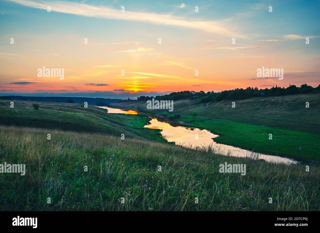 Sommerlandschaft mit Fluss fließt zwischen den grünen Hügeln auf einem Hintergrund von bunten Sonnenuntergang Himmel. Stockfoto