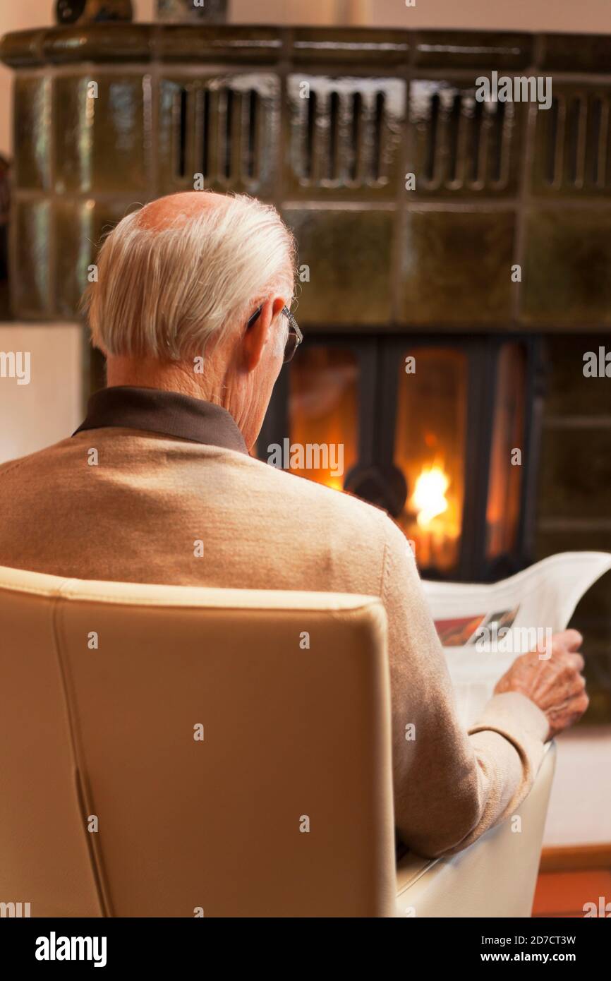 Ein alter Mann liest Zeitung, während er an einem Kamin sitzt Ein Wohnzimmer - selektiver Fokus auf den Kopf Stockfoto