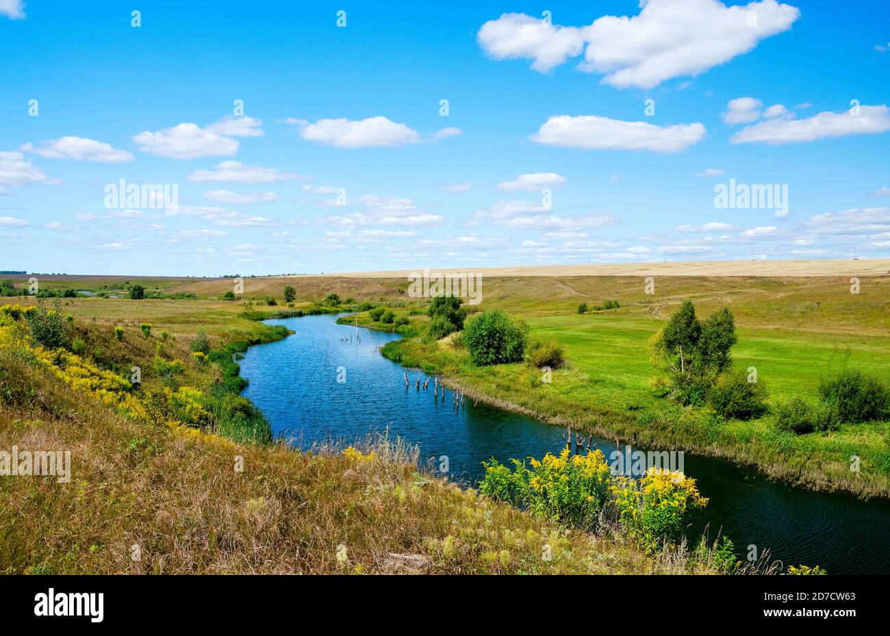 Sonnige Sommerlandschaft mit Fluss, der zwischen den schönen grünen Hügeln, Feldern und Wiesen fließt. Stockfoto