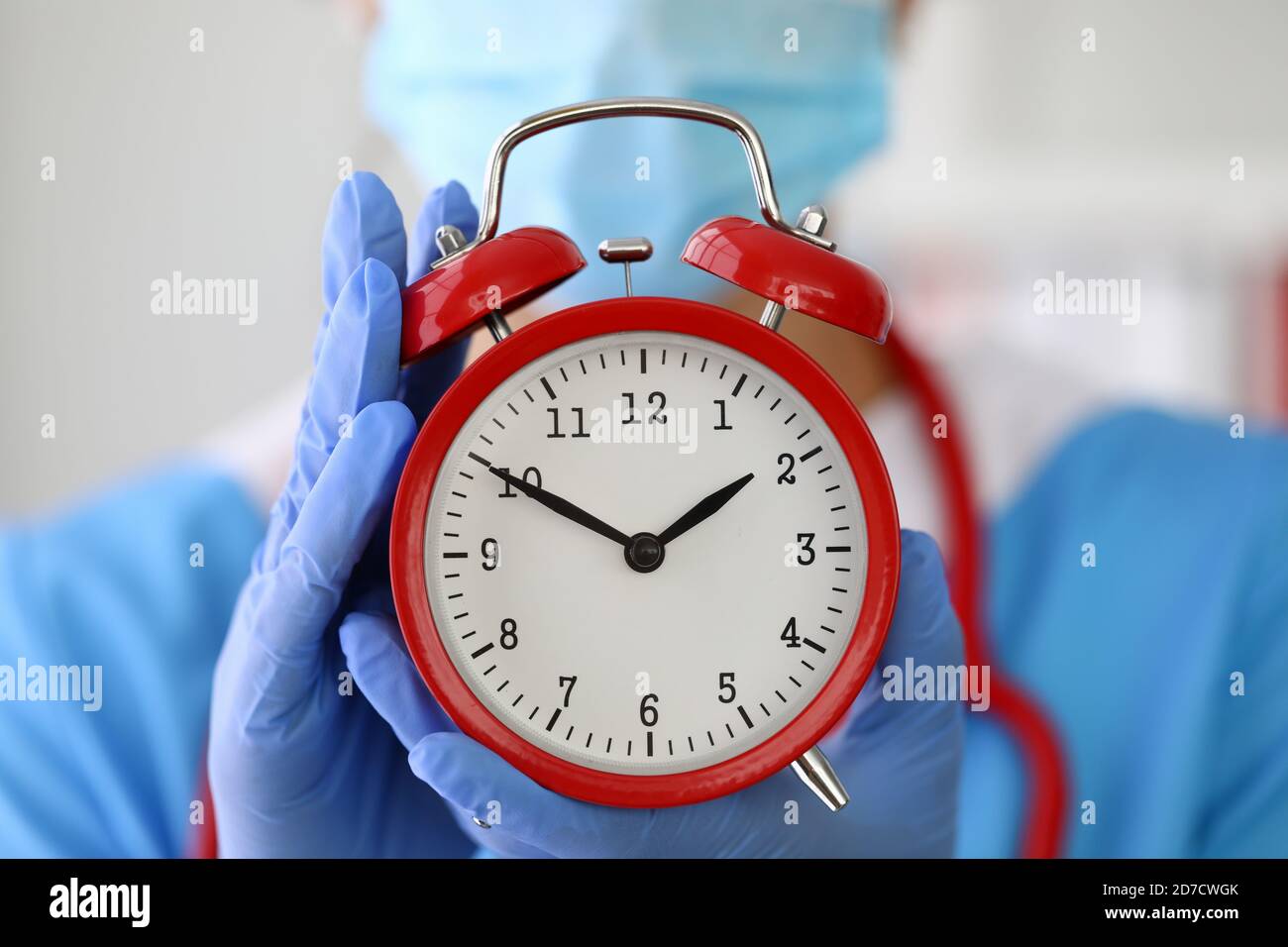 Arzt in Handschuhen hält roten Wecker Nahaufnahme. Stockfoto