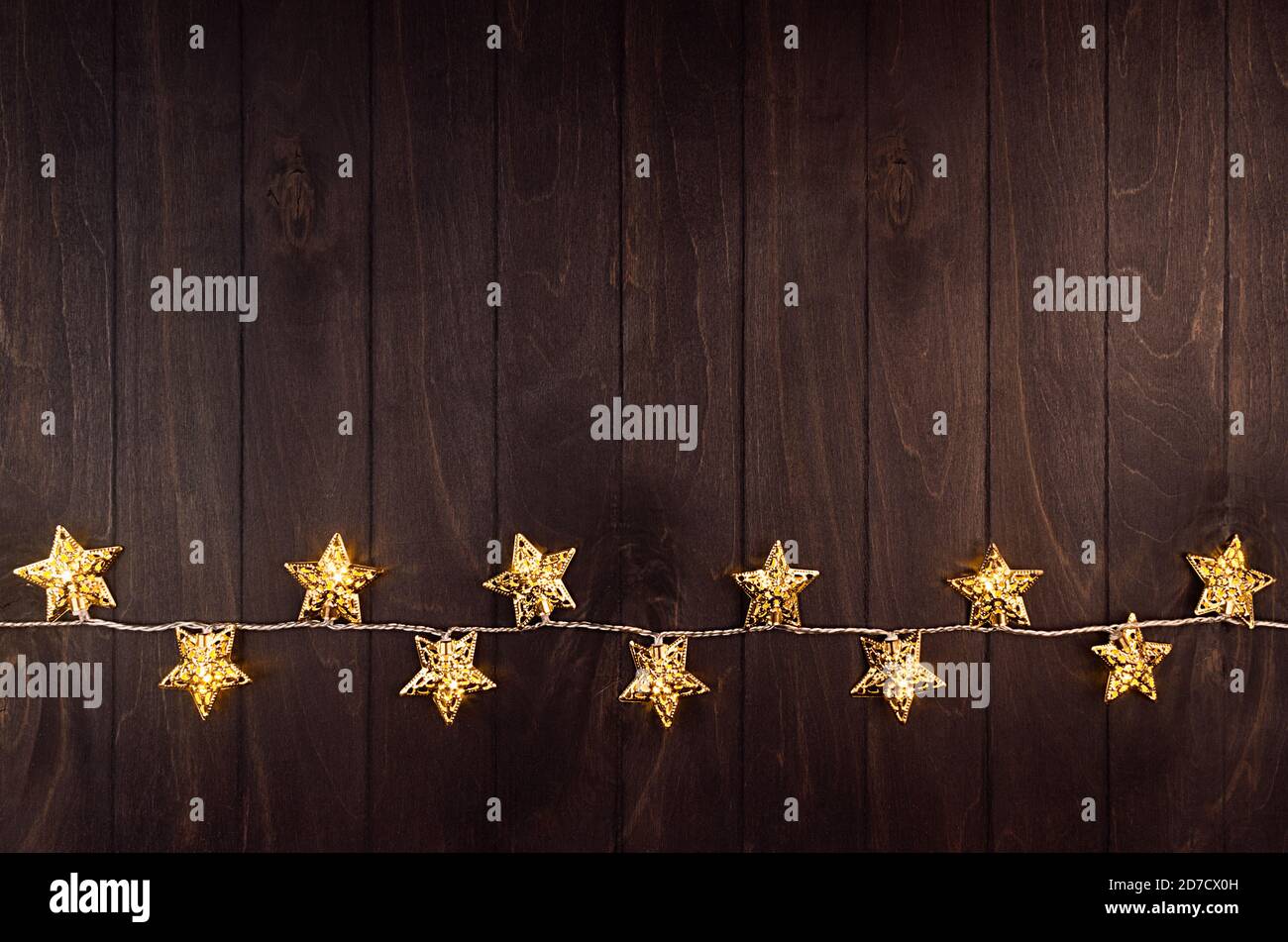 Weihnachtsdekoration - goldene Sterne auf Lichtern Girlande glühen auf dunkelbrauner Planke, Bordüre, Draufsicht, Kopierraum. Stockfoto