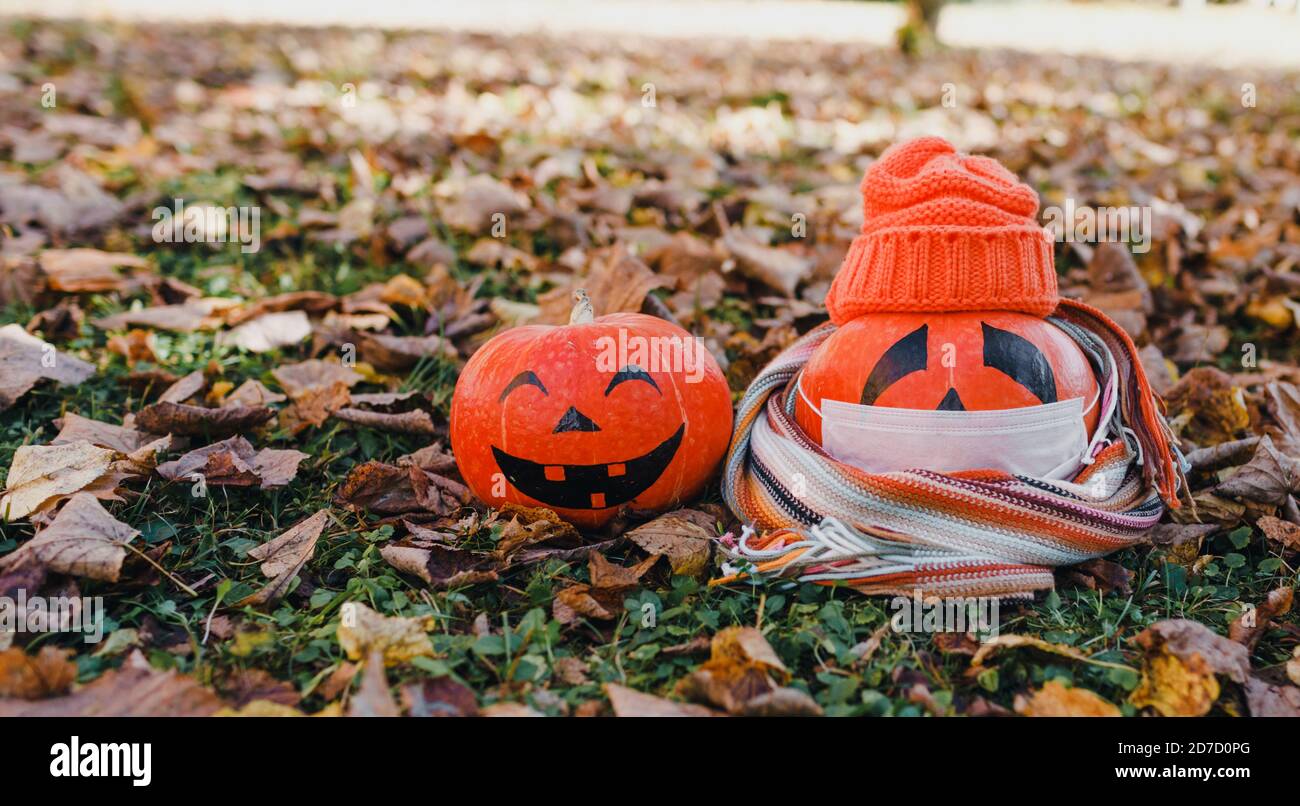 Zwei Kürbis der gesunde und der Kranke.Kürbis in einer Maske Und eine Strickmütze in orange Farbe auf bunten Herbst Blätter Stockfoto
