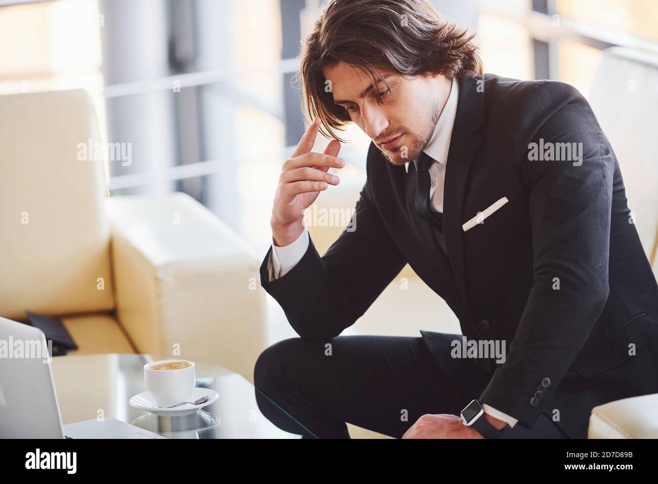 Sitzt auf dem Sofa. Porträt eines gutaussehenden jungen Geschäftsmannes in schwarzem Anzug und Krawatte Stockfoto