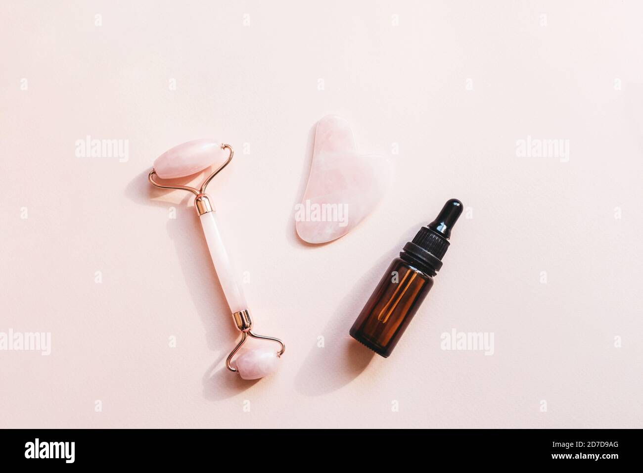 Massage-Roller, guasha und Gesichts-Serum auf rosa Hintergrund. Hautpflegeprodukte. Stockfoto