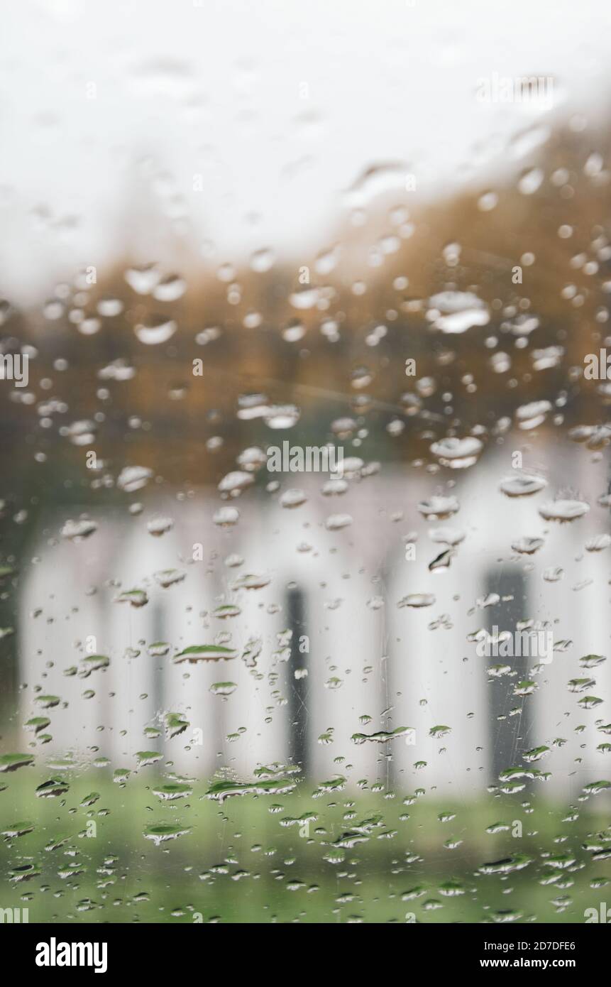 Verschwommene Ansicht der Reihe der weißen Häuser durch die Windschutzscheibe des Autos im regnerischen Herbstmorgen. Stockfoto
