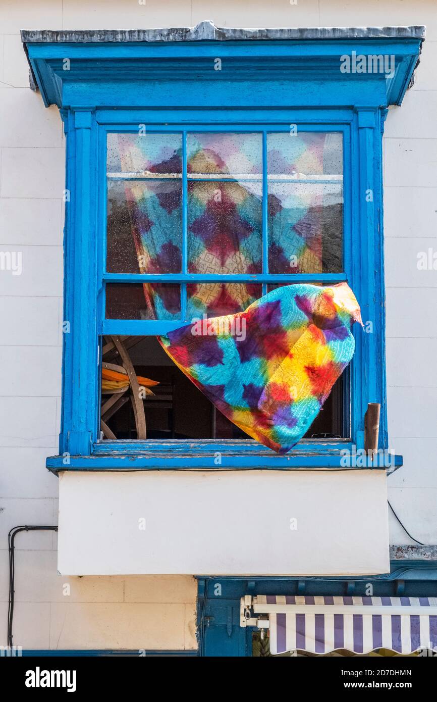 Ein knallfarbener Vorhang, der aus einem alten blauen Fenster oben wehte, ließ an einem windigen Tag in Großbritannien offen Stockfoto