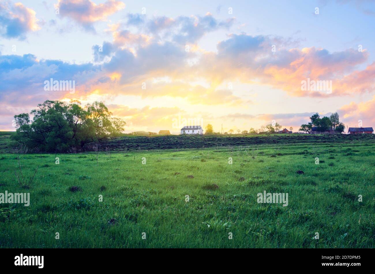 Leere grüne Wiese und weißes Landhaus auf einem Hintergrund der aufgehenden Sonne. Stockfoto