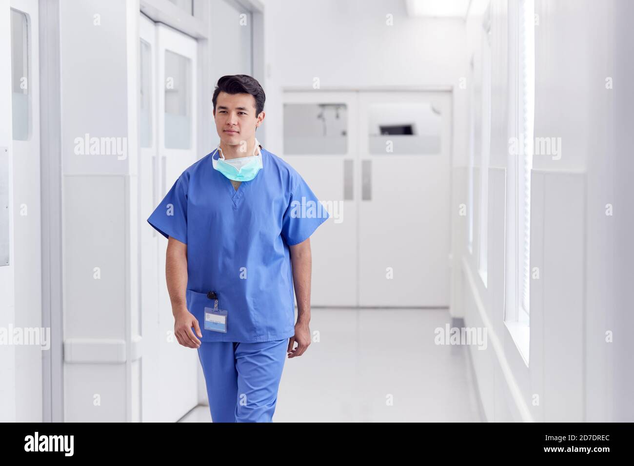 Junge Männliche Arzt Trägt Scrubs Zu Fuß Entlang Krankenhaus Korridor Stockfoto