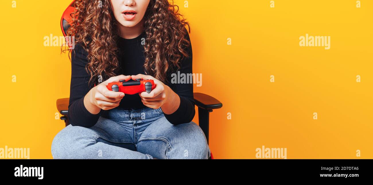 Frau, die hinter einem Spielstuhl in ihren Händen sitzt und rot hält Gamepad auf gelbem Hintergrund Stockfoto